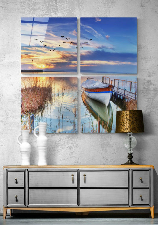 Four-panel glass wall art displaying lakeside and coastal scenes with sunsets, boats, and reeds, displayed above a mid-century dresser.