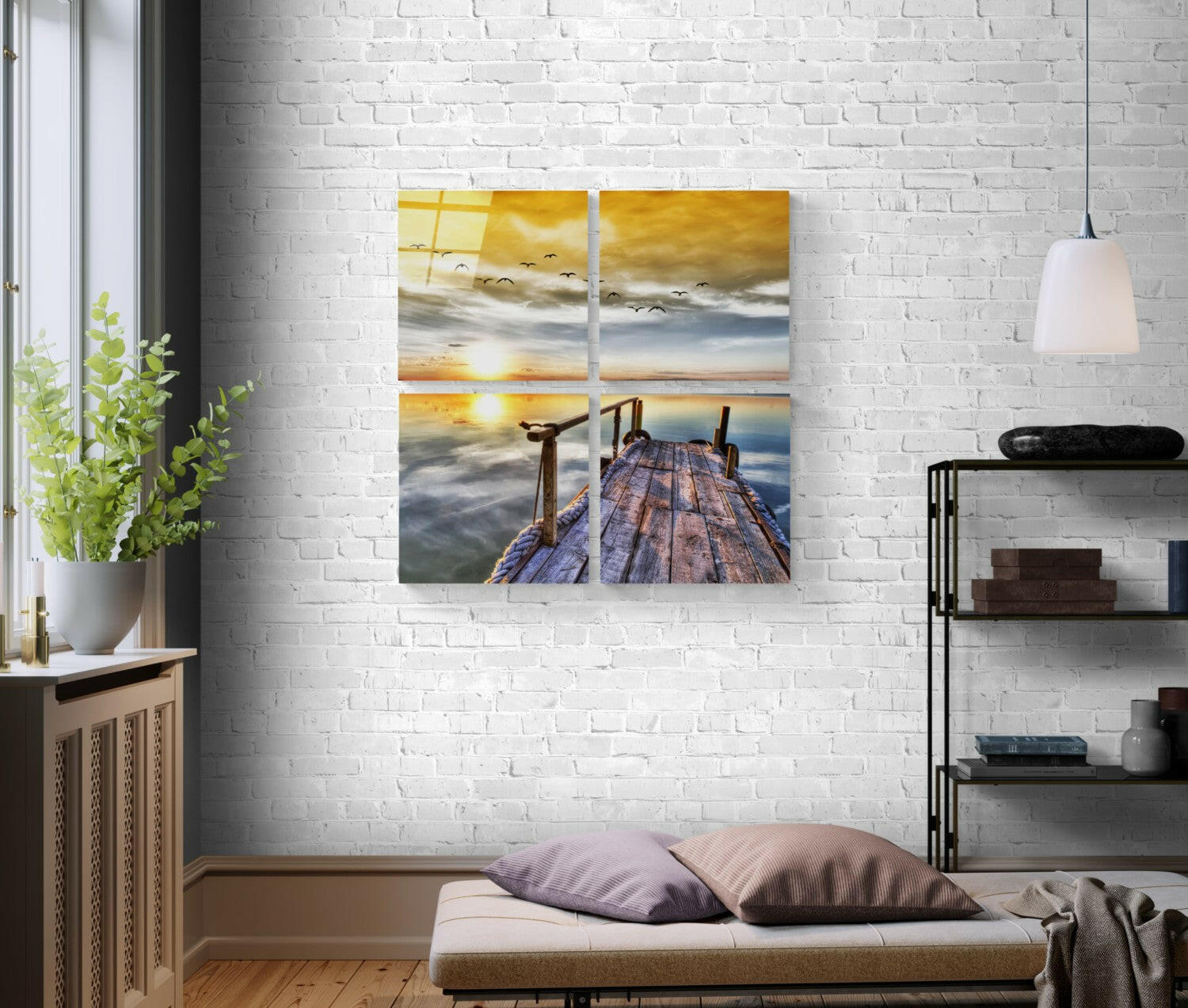 Four-panel glass wall art displaying a wooden pier at sunset with golden sky, birds, and calm water, mounted on white brick wall above bedroom bench.