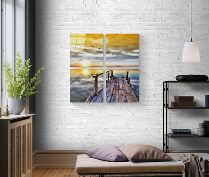 Four-panel glass wall art displaying a wooden pier at sunset with golden sky, birds, and calm water, mounted on white brick wall above bedroom bench.