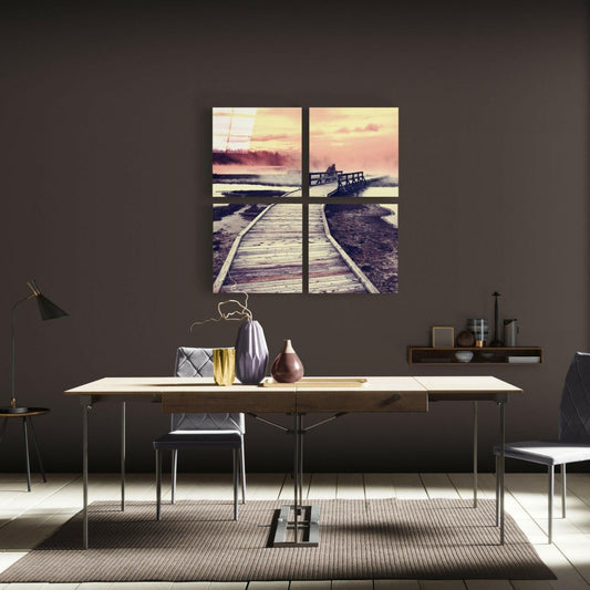 Four-panel glass wall art depicting a wooden boardwalk leading to a sunset over water, displayed above a desk in a modern interior.