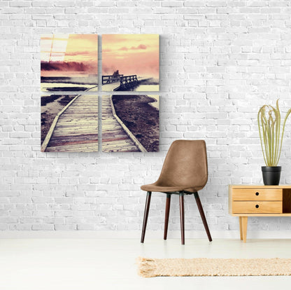 Four-panel glass wall art depicting a wooden boardwalk extending toward a sunset over water with warm golden and pink tones.