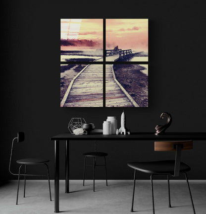 Four-panel glass wall art hung above a black desk showing wooden boardwalks and docks at sunset in warm amber and pink tones.