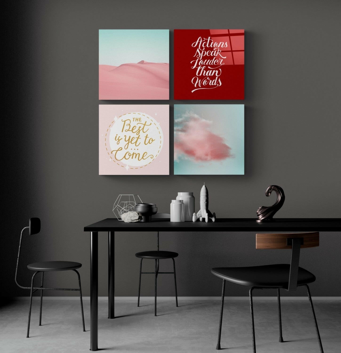 Four glass wall art panels in a 2x2 grid above a black desk, featuring desert landscapes, motivational quotes in script, and pink cloud imagery.