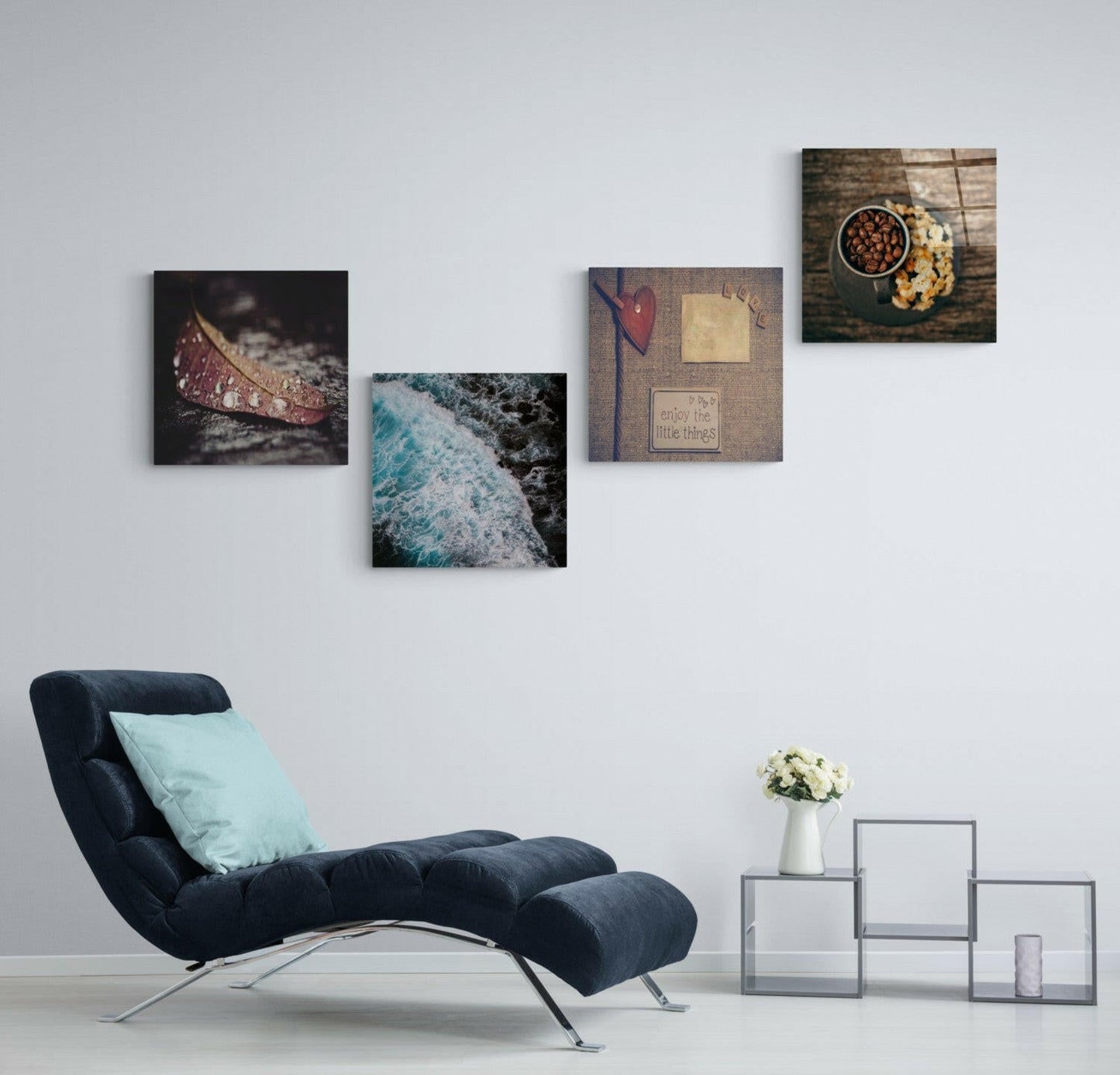 Four glass wall art prints displayed on light gray wall above navy chair, including coastal waves, leaf detail, and motivational text design.