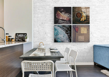 Four-panel glass wall art mounted on white brick above dining table, featuring food, nature, and inspirational text imagery in warm and cool tones.
