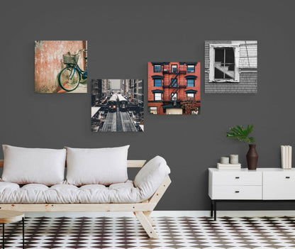 Modern living room with gray wall displaying four urban photography glass art prints above a wooden sofa with white cushions.