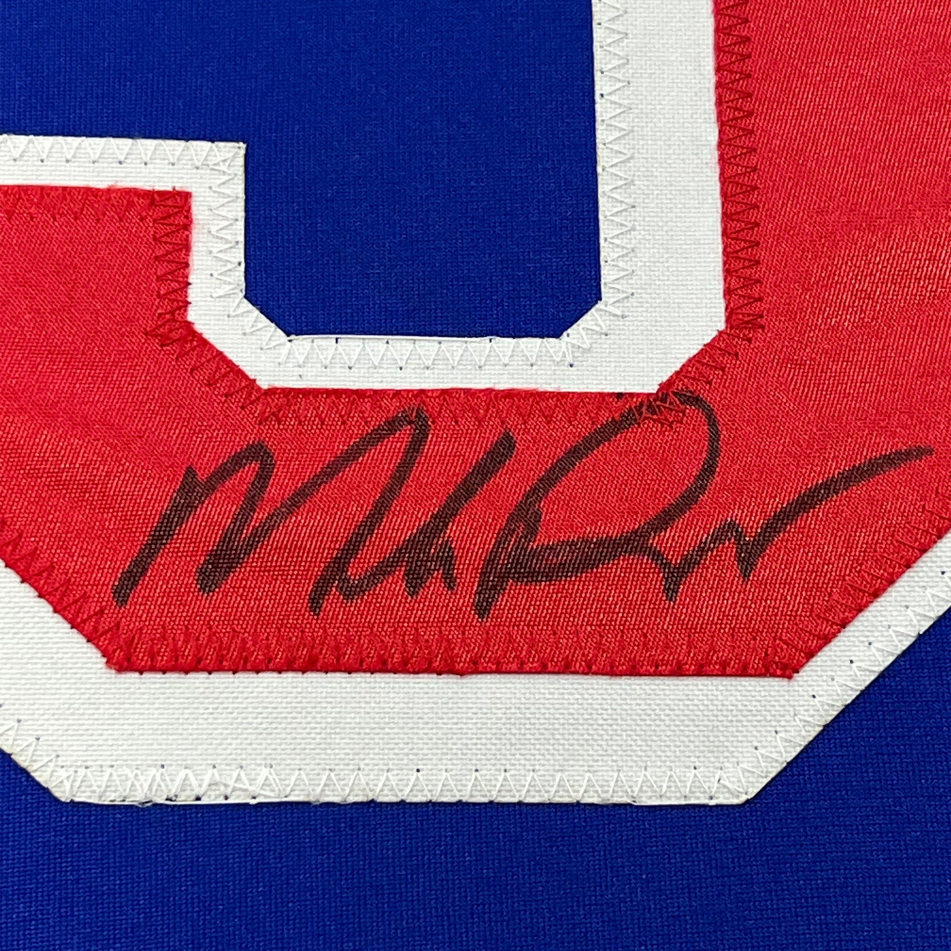 Close-up of autographed red chest stripe on blue New York Rangers hockey jersey showing handwritten signature.