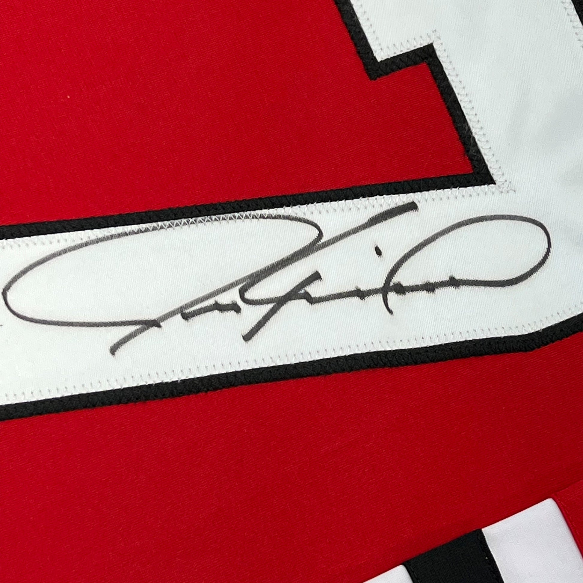Close-up of autographed signature in black ink on white stripe of red and black hockey jersey.