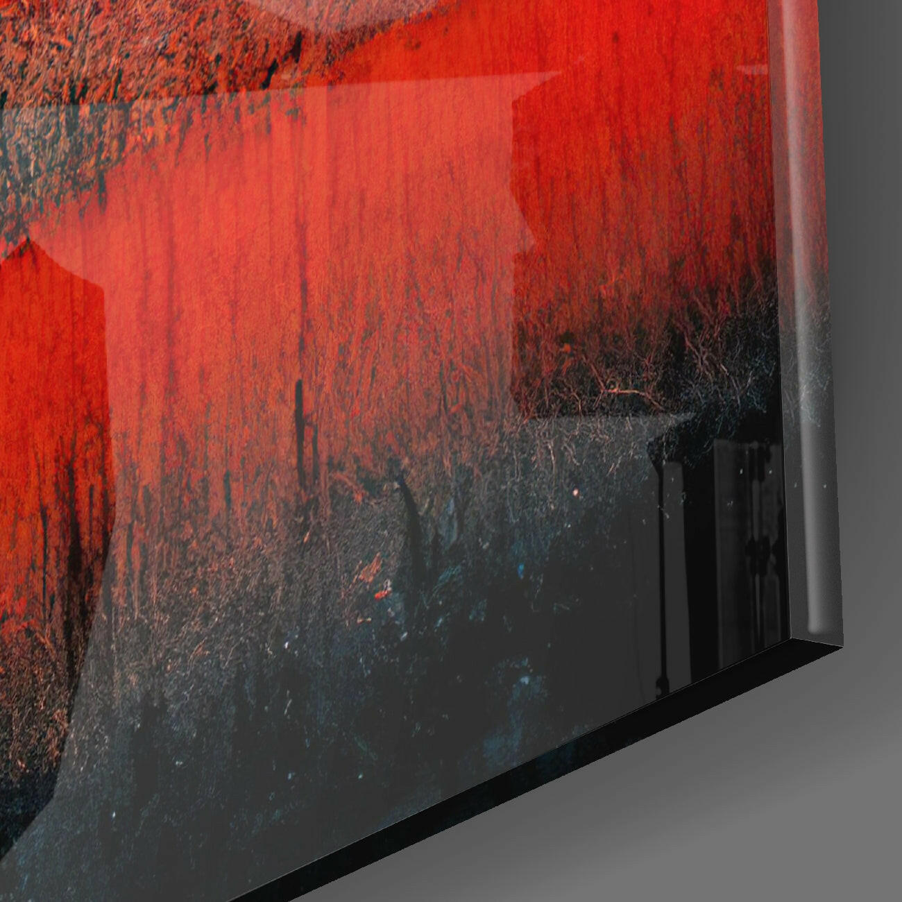 Close-up angled view of glass wall art showing red and black textured surface with dark frame edge against gray background.