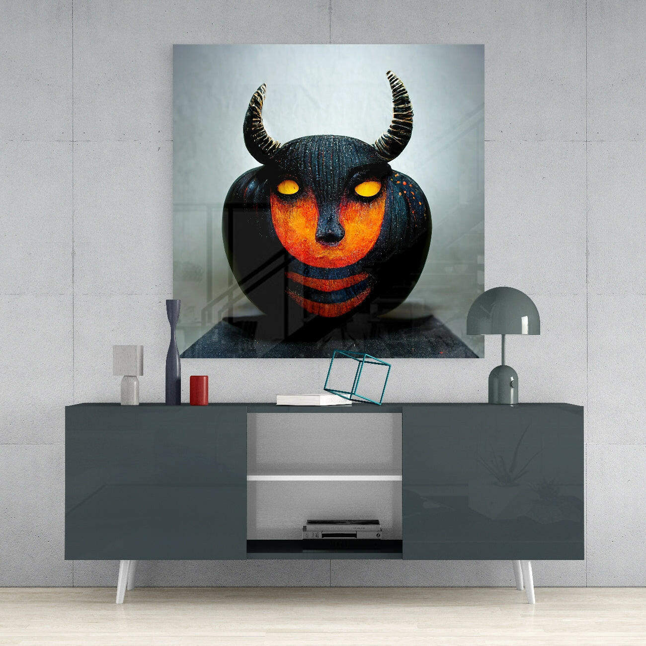 Black glass wall art with glowing orange face, yellow eyes, and curved horns displayed above a dark console table in a modern interior setting.