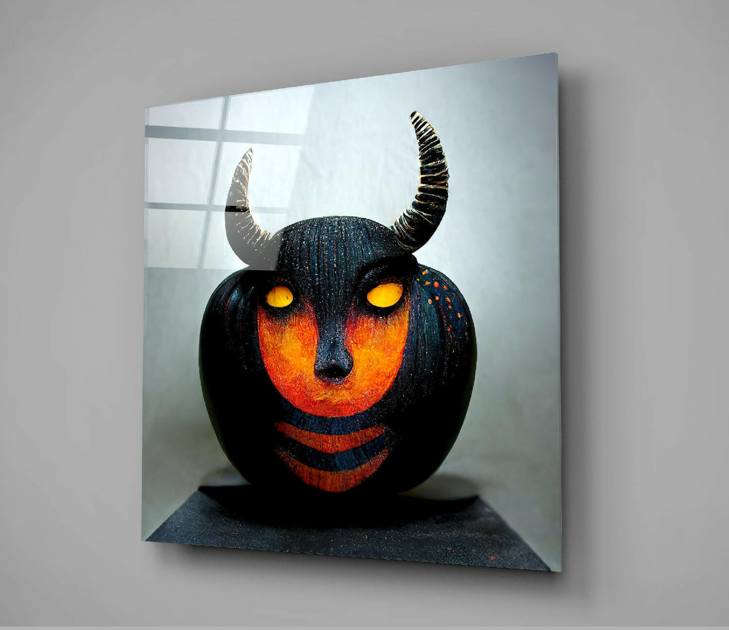 Black spherical sculpture with glowing orange face, yellow eyes, and curved horns mounted on glass panel against light background.