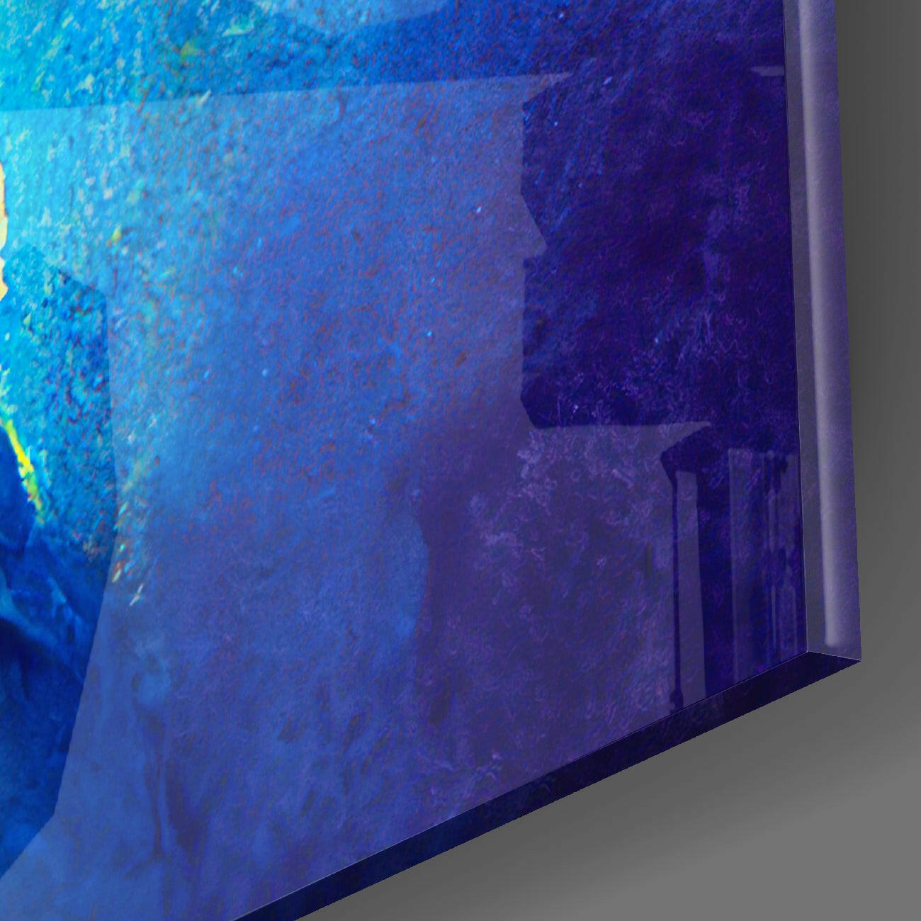 Blue glass wall art panel photographed at an angle, showing textured surface with gradient from bright cyan to deep indigo, mounted edge visible against gray wall.