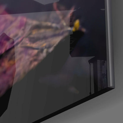 Close-up detail of yellow mask design on dark glass wall art panel with pink fabric visible at edge.