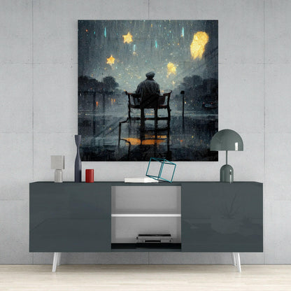 Glass wall art depicting a silhouetted figure on a chair gazing at glowing yellow stars and rain against a dark stormy sky, displayed above a modern gray media console.