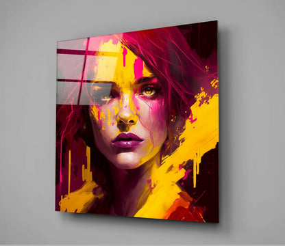 Modern glass wall art featuring a stylized female portrait in vibrant magenta, yellow, and pink tones with geometric overlay elements, mounted on a gray wall.