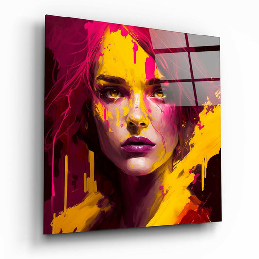 Angled view of glass wall art featuring a woman's face with vibrant magenta, yellow, and pink paint splatter effects against dark background.