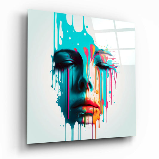 Glass wall art displaying a colorful melting face with turquoise, pink, and orange drips against white background, mounted at angle.