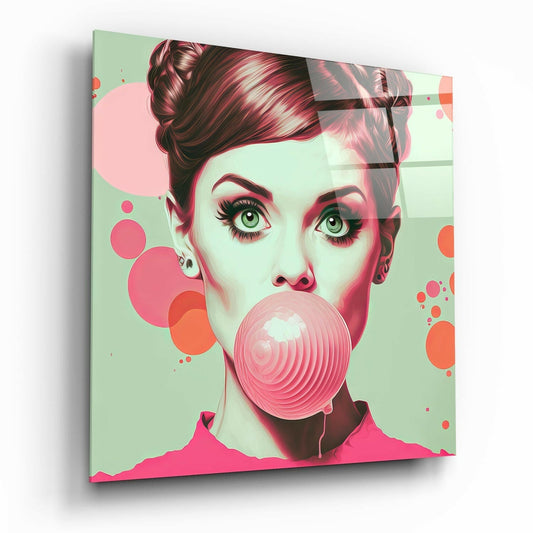 Angled three-quarter view of glass wall art showing a vintage-styled woman's face blowing a large pink bubble against a mint green and coral background with geometric circles.