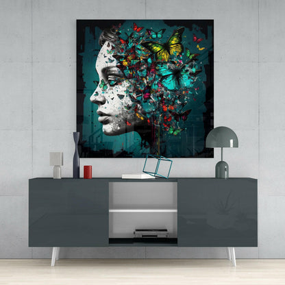 Glass wall art depicting a monochrome sculptural profile with colorful butterflies dispersing across teal background, displayed above gray media console.