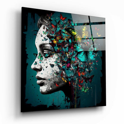 Glass wall art showing a white sculptural profile with colorful butterflies emerging from the head against a teal background, displayed at an angle.