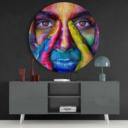 Vibrant circular glass wall art depicting a colorful human face with rainbow paint strokes, displayed above a gray modern console table with decor.
