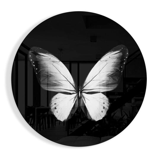Black and white photograph of a white butterfly with dark wing tips displayed on a circular black glass wall art piece.