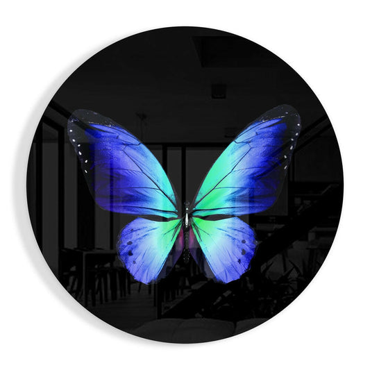 Vibrant blue and turquoise butterfly displayed on circular black glass wall art, mounted indoors against blurred background.