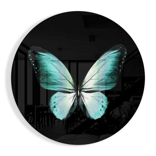 Turquoise and cream butterfly displayed on circular black glass wall art, photographed straight-on against a blurred interior background.