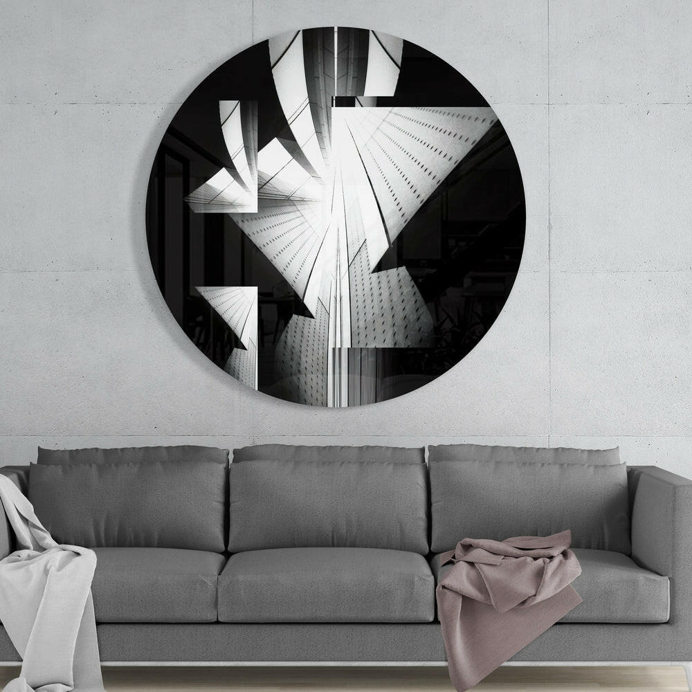 Circular black and white glass wall art depicting upward-angled skyscrapers mounted above a gray three-cushion sofa.