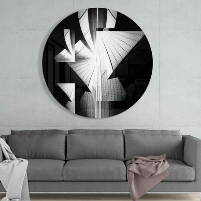 Circular black and white glass wall art depicting upward-angled skyscrapers mounted above a gray three-cushion sofa.