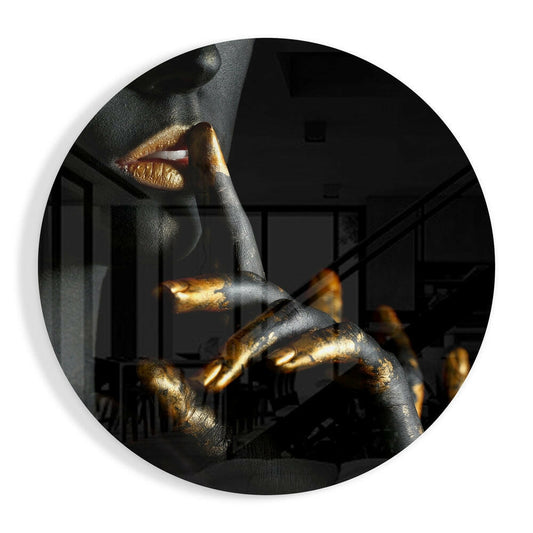 Round glass wall art featuring a figure with gold-painted lips and fingers against black skin tone, displayed indoors.