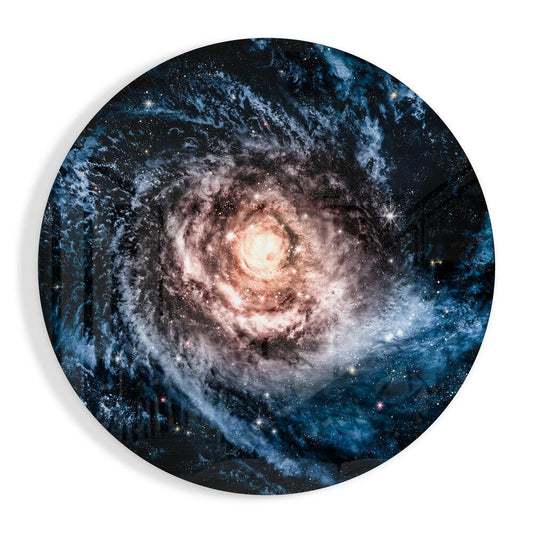 Circular glass wall art displaying a spiral galaxy with a bright central core surrounded by blue and pink dust lanes against a starry black background.