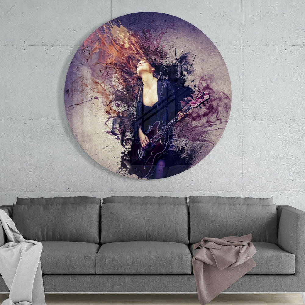 Circular glass wall art depicting a musician with a guitar surrounded by purple and gold watercolor splatter effects, mounted above a gray sofa.