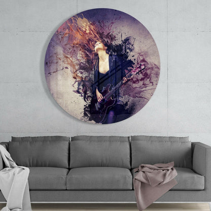 Circular glass wall art depicting a musician with a guitar surrounded by purple and gold watercolor splatter effects, mounted above a gray sofa.
