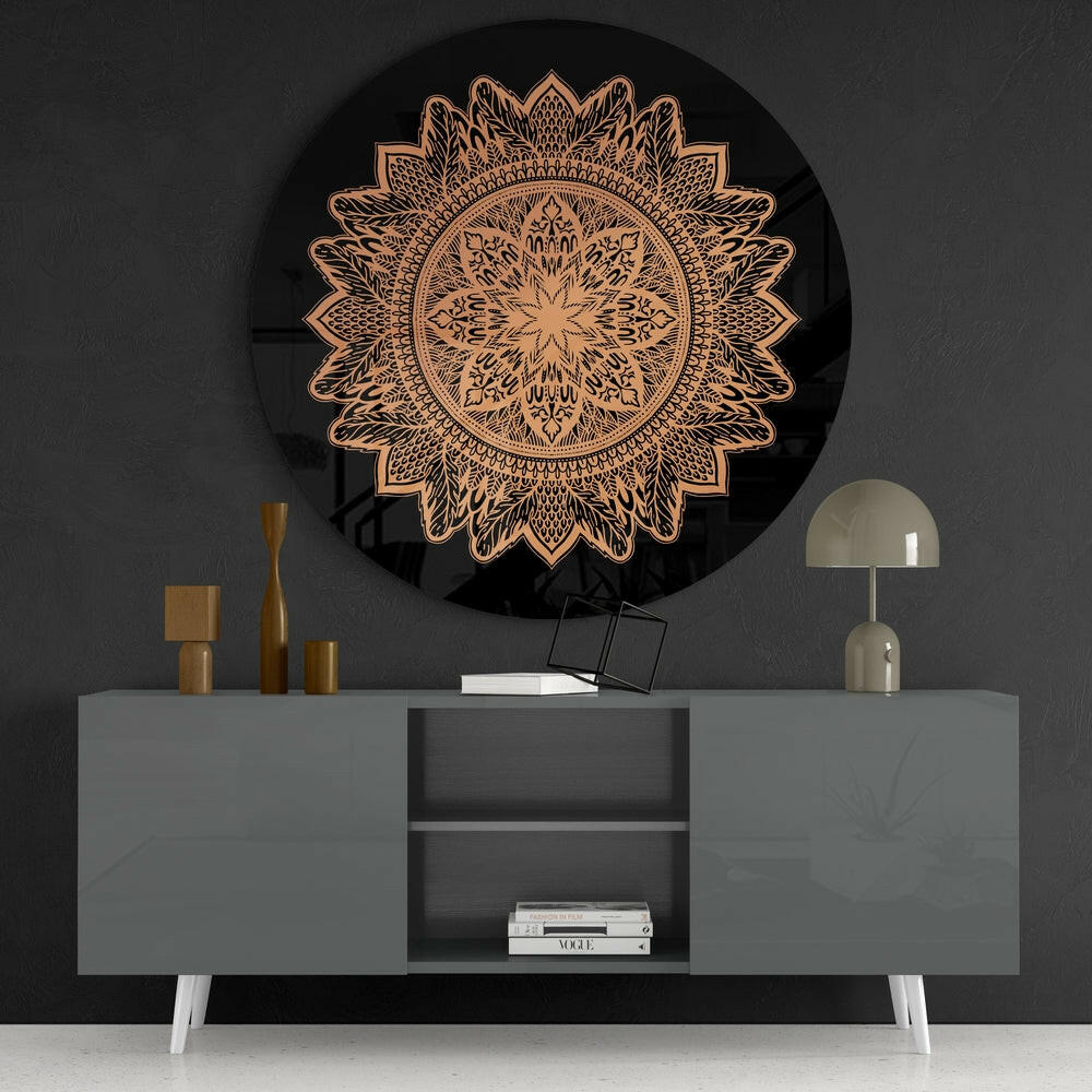 Round black glass wall art with copper-colored intricate floral mandala pattern displayed above gray console table with decor.