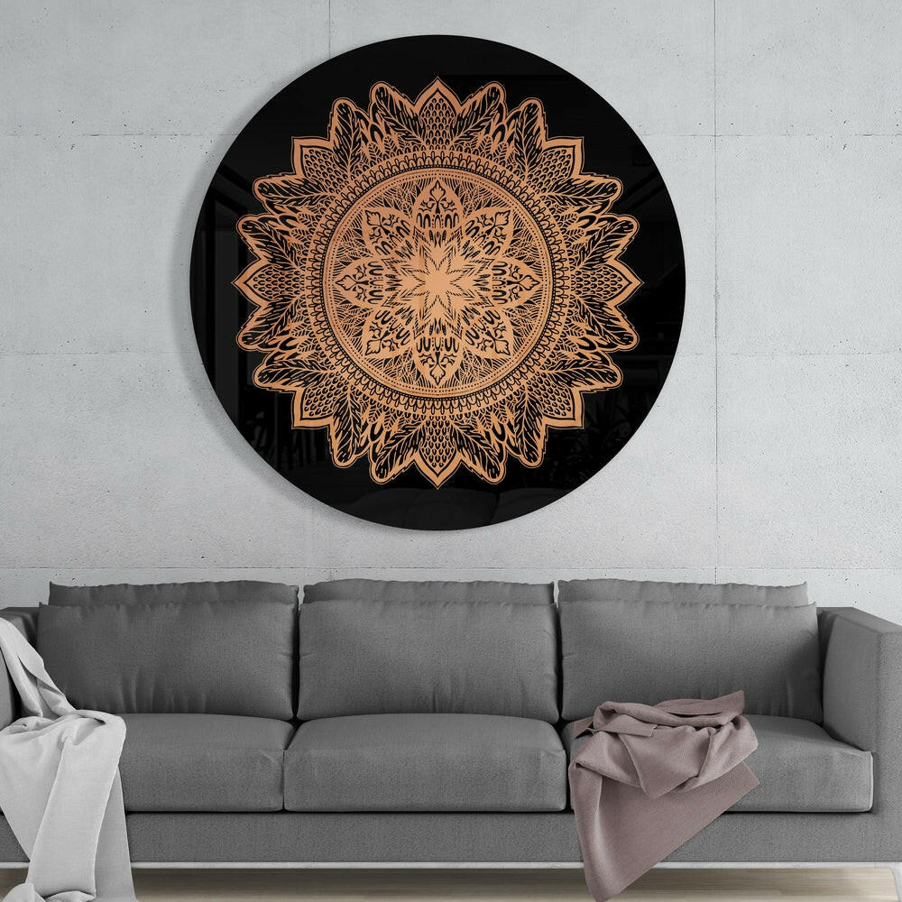 Black circular glass wall art with intricate copper-colored mandala flower pattern displayed above gray sofa in modern interior.
