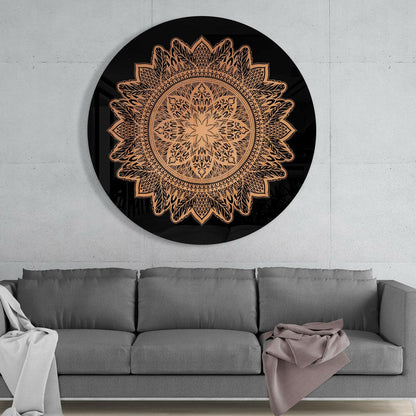 Black circular glass wall art with intricate copper-colored mandala flower pattern displayed above gray sofa in modern interior.