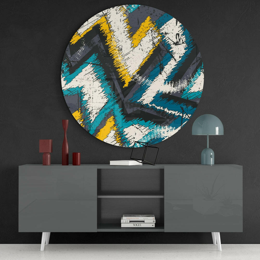 Circular glass wall art with turquoise, yellow, white and grey brushstroke pattern displayed above grey console table with red vases and teal lamp.