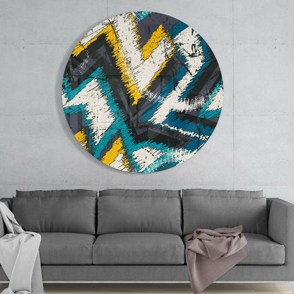 Round glass wall art with diagonal teal, yellow, cream, and charcoal brushstroke pattern displayed above gray sofa.