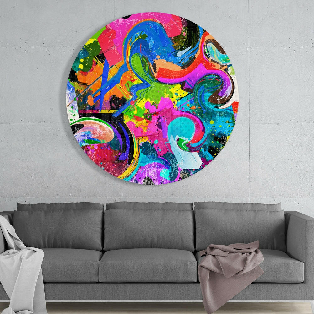 Vibrant circular glass wall art with swirling blue, pink, green, and orange patterns hung above a gray sofa against white wall.