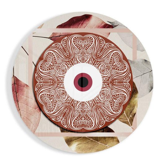 Terracotta ornate eye disc with white intricate patterns and burgundy iris center, surrounded by dried leaves in rust and gold tones on circular glass.