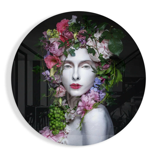 Pale woman's face adorned with pink, purple, and white flowers and green foliage, printed on circular glass with dark interior background.