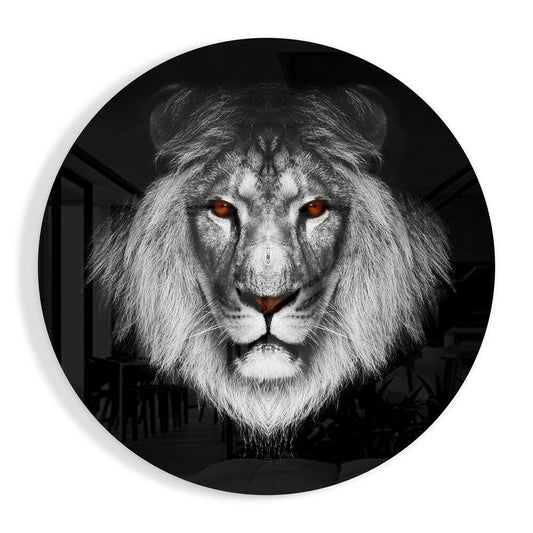 Circular glass wall art featuring a frontal lion head portrait in grayscale with glowing amber eyes against a dark background.