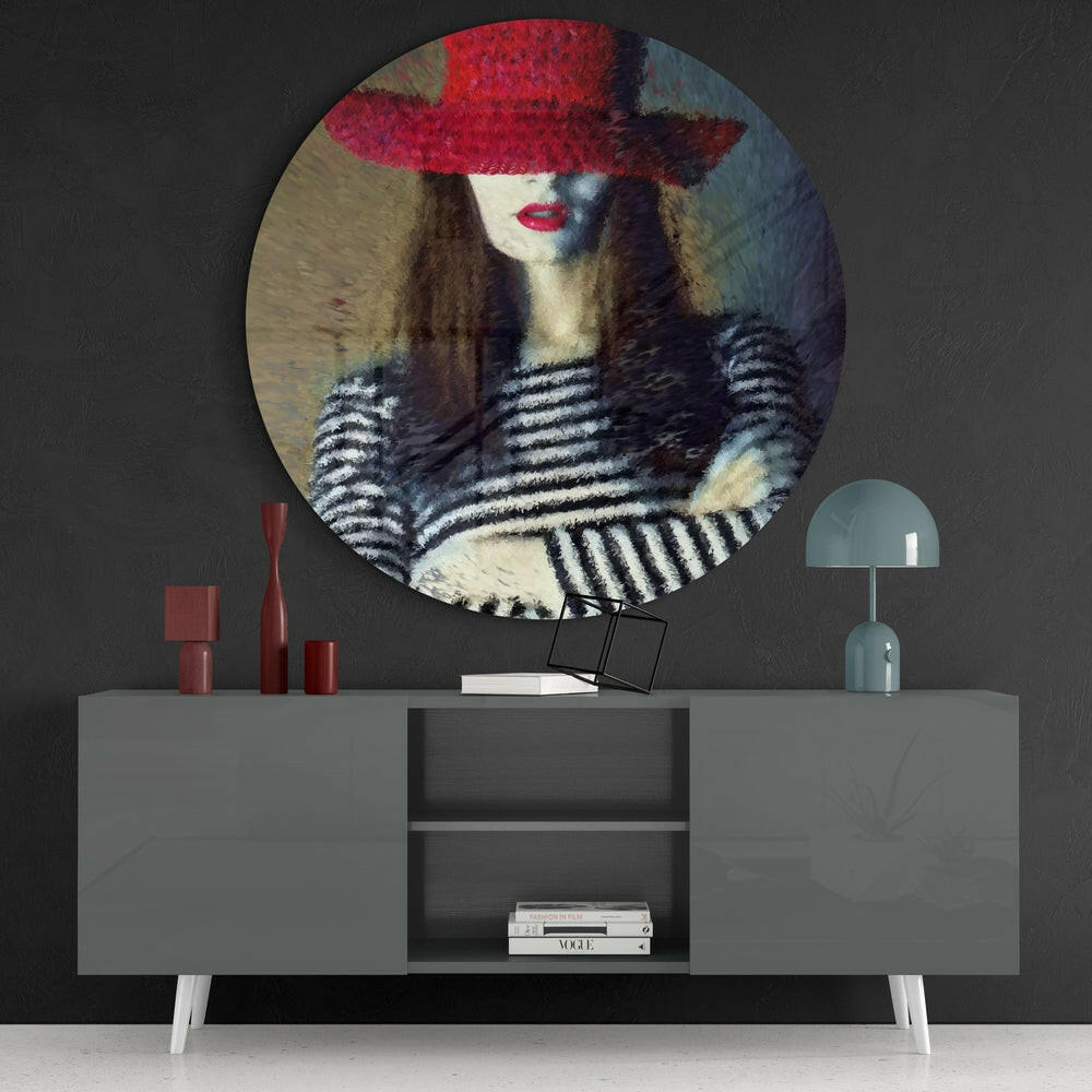 Circular glass wall art depicting a woman wearing a red hat and striped top displayed above a gray credenza with decorative accessories.