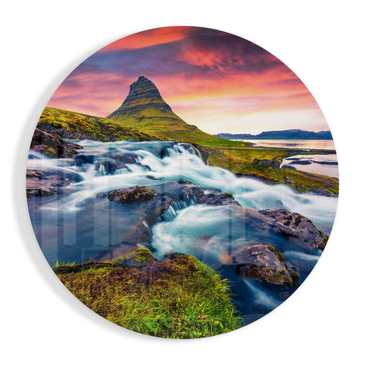 Circular glass wall art featuring a cascading waterfall beneath a cone-shaped mountain at sunset with vibrant pink and orange sky.