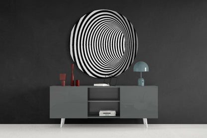 Black and white concentric circular glass wall art displayed above gray sideboard with red candles and teal lamp.