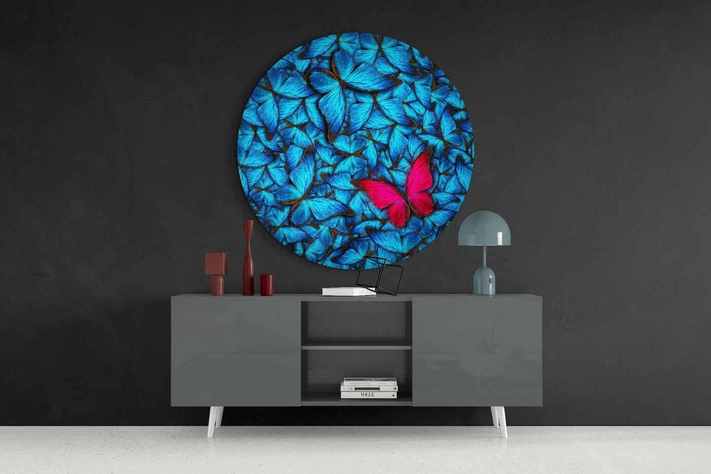 Circular glass wall art featuring blue butterflies with a single bright pink butterfly, displayed above a gray sideboard with decorative accessories.