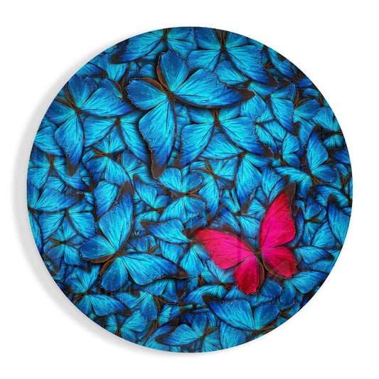 Circular glass wall art featuring a dense pattern of bright blue butterflies with one vibrant red-pink butterfly centered among them.
