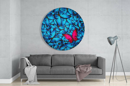 Round glass wall art displaying blue butterflies with one red butterfly, mounted above gray sofa in minimalist interior.