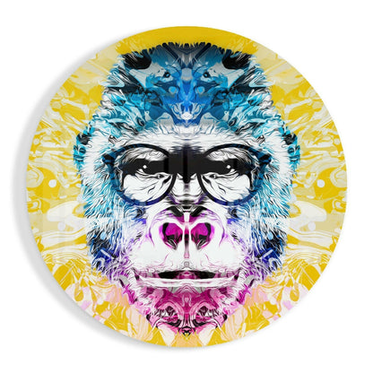 Circular glass wall art featuring a stylized primate face with blue, pink, and yellow colorwork and large black-rimmed glasses.